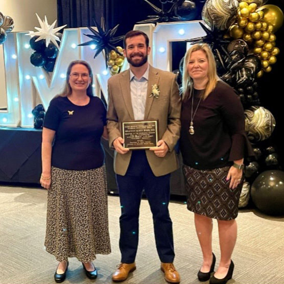 Jonathan Austin Berry stands with two faculty members holding an award.